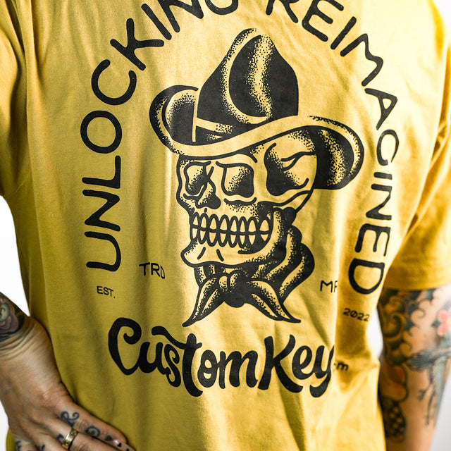 Tattooed woman wearing a yellow t-shirt with skull with cowboy hat and 'CustomKeys.com' text on a white background